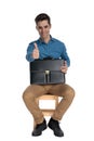 Happy young man making thumbs up sign and holding suitcase Royalty Free Stock Photo