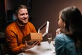 Happy young man opening box with received gift from loving girlfriend and looking to her enjoying romantic dinner date Royalty Free Stock Photo