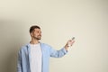 Happy young man operating air conditioner with remote control on beige background. Space for Royalty Free Stock Photo