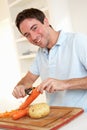 Happy young man peeling vegetable in kitchen