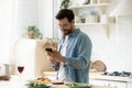 Happy young man preparing romantic dinner using smartphone app Royalty Free Stock Photo