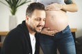 A Happy young man putting ear to pregnant womans belly listening to baby moving inside.