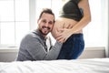 A Happy young man putting ear to pregnant womans belly listening to baby moving inside.