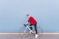 Happy young man in a red sweatshirt sitting on a white bike against a blue wall background Royalty Free Stock Photo