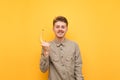 Happy young man in shirt and glasses stands on yellow background with banana in hand, looks into camera with serious face. Funny Royalty Free Stock Photo