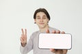 Happy young man showing two fingers and modern smartphone with empty white display on white background. Sale and great offer