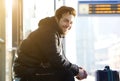 Happy young man sitting with bag at train station Royalty Free Stock Photo