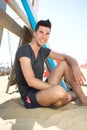 Happy young man sitting at the beach with surf board Royalty Free Stock Photo