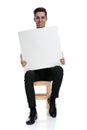 Happy young man sitting on chair and holds blank board Royalty Free Stock Photo