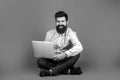 Happy young man sitting on the floor with and using laptop computer. Holding laptop computer. Smiling handsome bearded Royalty Free Stock Photo