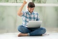 Happy young man sitting on floor working with laptop computer raise  fist celebrating to succes  on window at home  . excited male Royalty Free Stock Photo