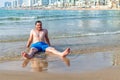 Happy young man sitting on a sandy beach with buildings in the background Royalty Free Stock Photo