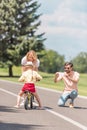 happy young man with smartphone photographing smiling mother teaching daughter riding bicycle
