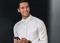 Happy young man smiling, texting messages from his cellphone over studio black background, with wireless earphones. Royalty Free Stock Photo
