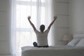 Happy young man stretching in bed after waking up, back view Royalty Free Stock Photo