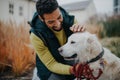 Happy young man stroking his dog outdoors in city park, during cold autumn day. Royalty Free Stock Photo
