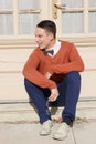 Happy young man in sweater sitting on steps in front of house Royalty Free Stock Photo