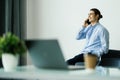 Happy young man talking on cell phone and using laptop in office Royalty Free Stock Photo