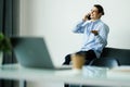 Happy young man talking on cell phone and using laptop in office Royalty Free Stock Photo