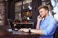 Happy young man talking on phone while using laptop at outdoor cafe Royalty Free Stock Photo