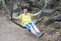 Happy young man, the teenager, the tourist, shakes on a liana as on a swing on Beng Mealea temple ruin in the Koh Ker complex, Si Royalty Free Stock Photo