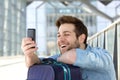 Happy young man with traveling bag looking at cell phone Royalty Free Stock Photo