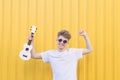 Young man with ukulele in his hands poses against the background of the yellow wall. Musical concept