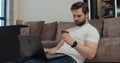 Happy young man using credit card and laptop computer in living room, online shopping, order food delivery. Online Royalty Free Stock Photo