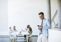 Happy young man using his mobile phone and smiling while his colleagues working in the background Royalty Free Stock Photo