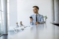 Happy young man using his mobile phone and smiling while his colleagues working in the background Royalty Free Stock Photo
