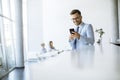 Happy young man using his mobile phone and smiling while his colleagues working in the background Royalty Free Stock Photo