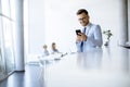 Happy young man using his mobile phone and smiling while his colleagues working in the background Royalty Free Stock Photo