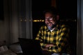 Happy young man using a laptop or computer at home working late night in the dark with the light of the screen on his face smiling Royalty Free Stock Photo