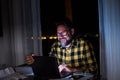 Happy young man using a laptop or computer at home working late night in the dark with the light of the screen on his face smiling Royalty Free Stock Photo