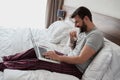 Happy man using laptop computer while sitting in bed Royalty Free Stock Photo