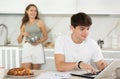Happy young man using laptop in the kitchen while communicating with his girlfriend Royalty Free Stock Photo