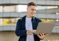 A happy young man using a laptop outdoors, dressed in a casual Royalty Free Stock Photo