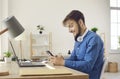 Happy young man using mobile phone while sitting at work desk with laptop at home Royalty Free Stock Photo