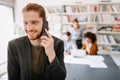 Happy young man using mobile phone and smiling while his colleagues working in office Royalty Free Stock Photo