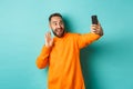 Happy young man video calling, talking online with mobile phone, saying hello to smartphone camera and waving hand Royalty Free Stock Photo