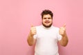 Happy young man in white t-shirt and overweight stands on a pink background and shows thumbs up with a smile on his face. Fat Royalty Free Stock Photo