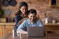 Happy young man and woman hugging, using laptop in kitchen Royalty Free Stock Photo