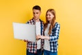 Happy young man and woman in a plaid shirt, using the laptop on a yellow background Royalty Free Stock Photo