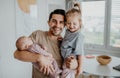 Happy young man taking care of his newborn baby and little daughter indoors at home, paternity leave