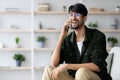 Happy middle eastern man sitting on sofa, talking on phone Royalty Free Stock Photo