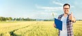 Young farmer standing in wheat field with clipboard, looking directly at camera and showing thumbs up