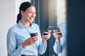 Happy young mixed race businesswoman browsing on a cellphone while drinking a cup of coffee at a window in an office Royalty Free Stock Photo
