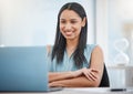 Happy young mixed race businesswoman smiling while enjoying working on a laptop sitting in a chair in an office at work Royalty Free Stock Photo