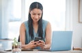 Happy young mixed race businesswoman smiling while using a phone and working on a laptop sitting in a chair in an office Royalty Free Stock Photo