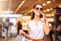 A happy young mixed race woman wearing sunglasses using a cell phone while carrying bags during a shopping spree. Young Royalty Free Stock Photo